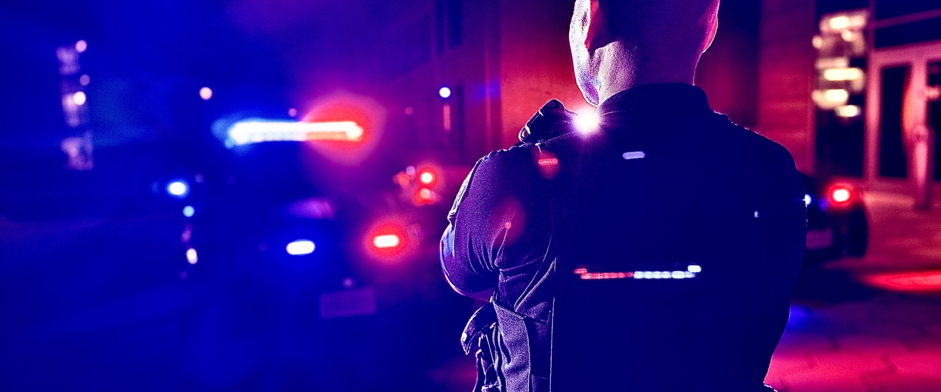 Image of a police officer standing in front a police vehicle with lights on