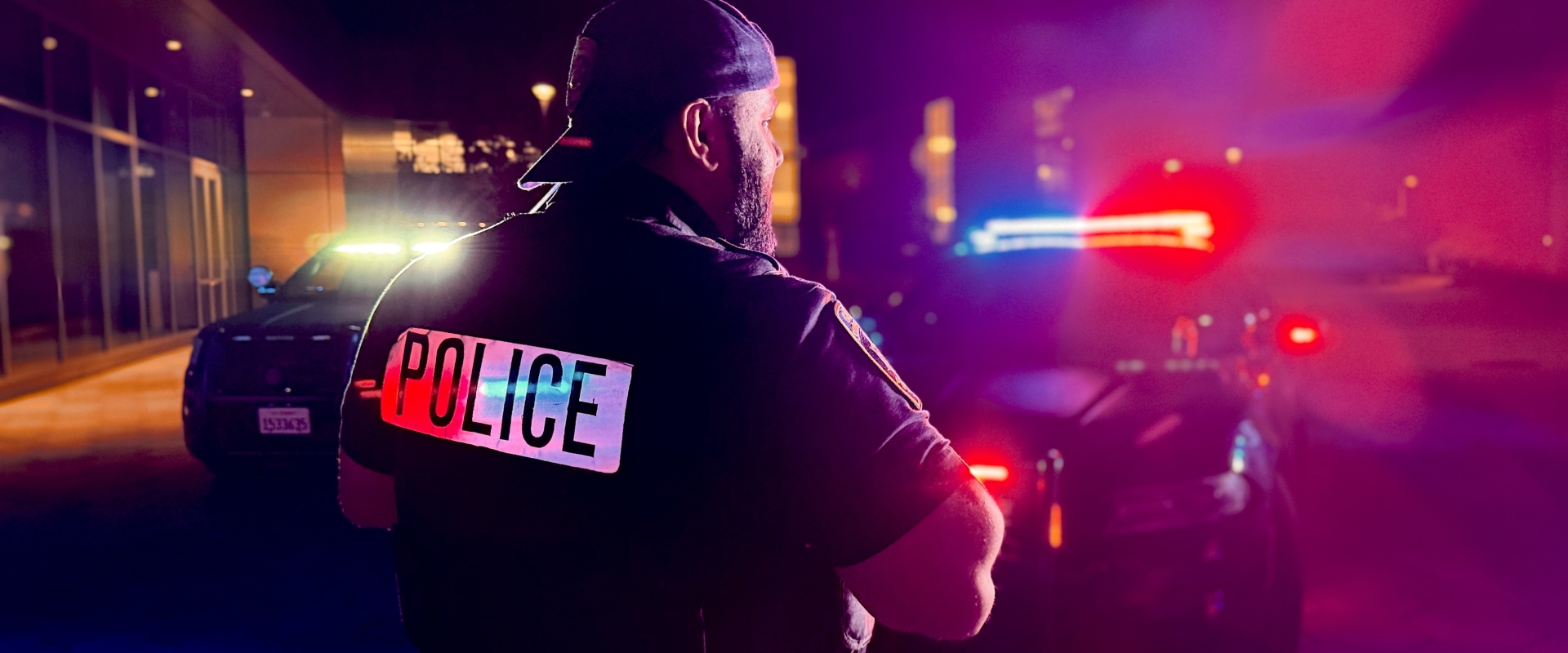 Image of back of UPD officer standing in front of UPD vehicles with patrol lights on 