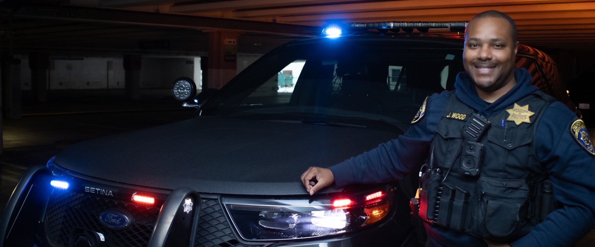 Image of UPD officer standing in front of UPD Police SUV with lights on
